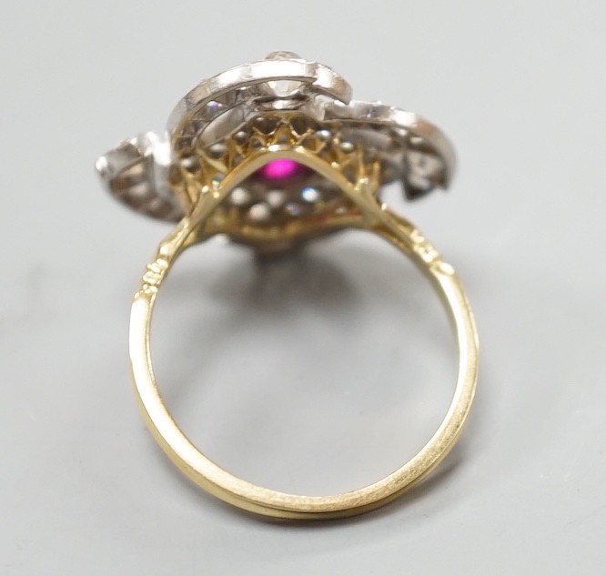 A yellow metal, ruby and diamond cluster set dress ring, in a pierced scroll setting, size O, gross weight 6 grams.